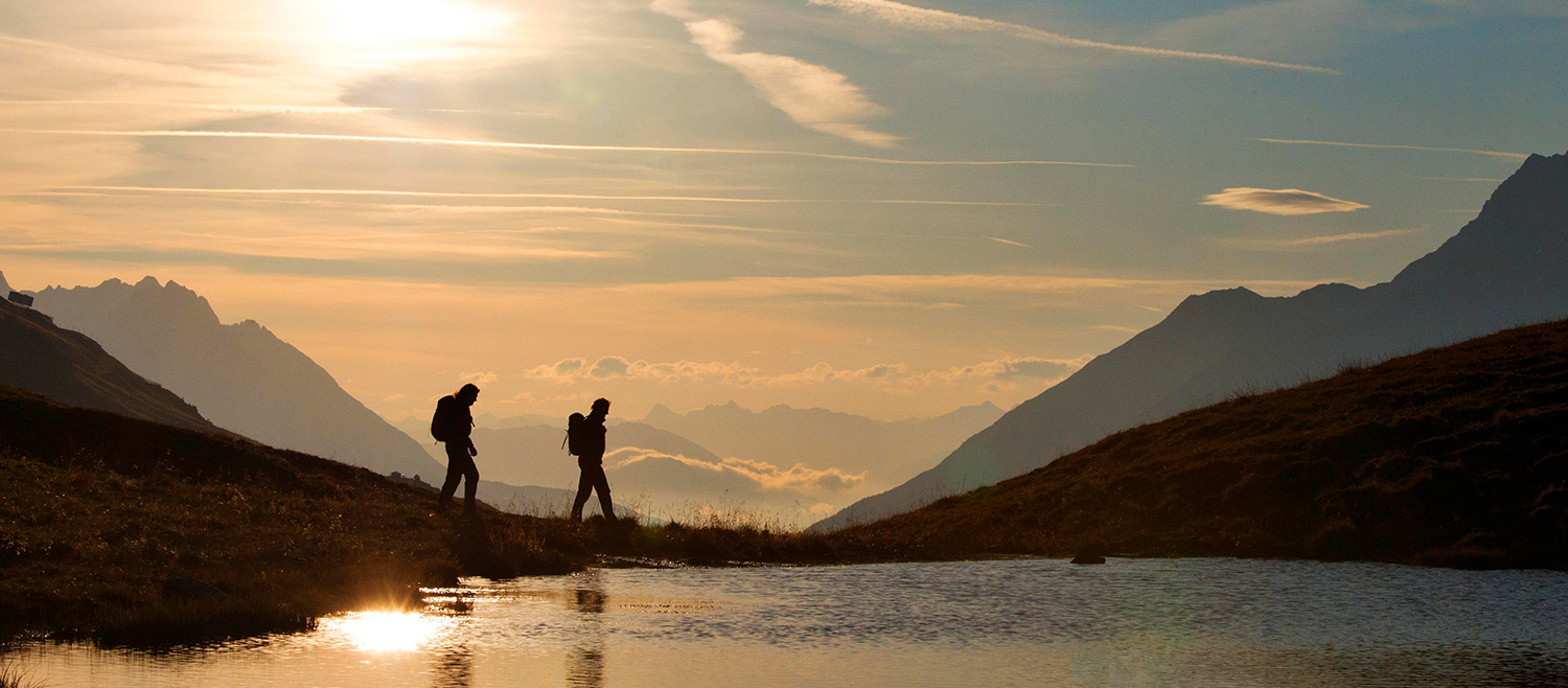 Wanderer am Bergsee bei Sonnenuntergang